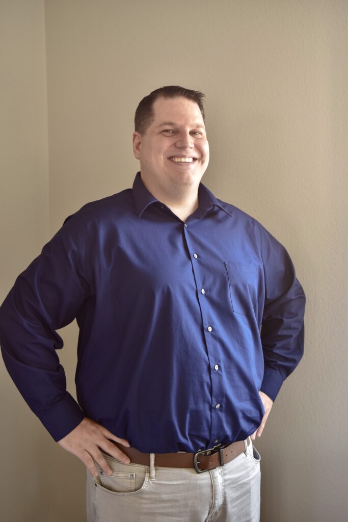 Smiling man in a blue shirt posing confidently indoors.